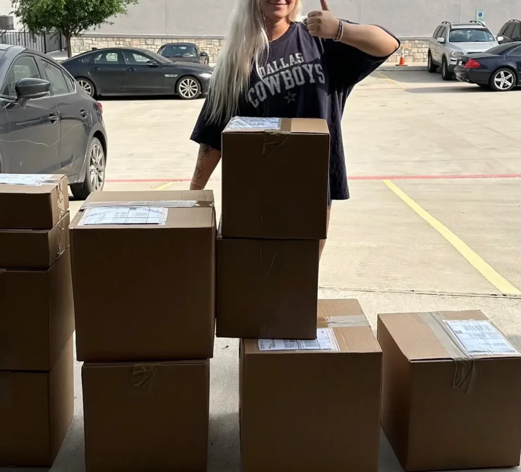 Happy Essential Group client giving a thumbs-up beside stacked cartons of a completed bulk clothing order ready for DDP shipment